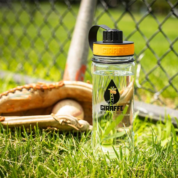 Giraffe Bottle Clear Tritan bottle filled with water next to a baseball glove and bat in fresh green grass