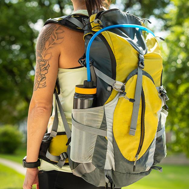 Person with a backpack outdoors using the Giraffe Bottle assistive hydration Journey system held by their backpack side pocket