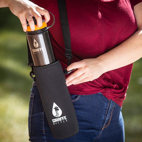 Person's hand sliding a shiny black stainless steel Giraffe Bottle into the black neoprene bottle carry bag with Giraffe Bottle logo